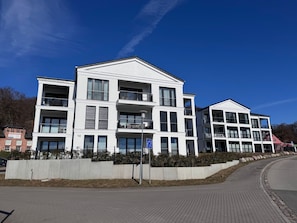 Ein modernes Mehrfamilienhaus mit Balkonen, einem gepflasterten Bürgersteig und blauem Himmel.