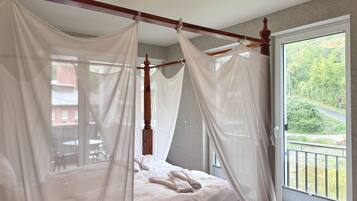 A four-poster bed with a canopy, a window with a view of greenery, and a ceiling light fixture.