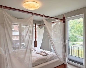 Ein Bett mit Baldachin, ein Fenster mit Blick ins Grüne und eine Deckenleuchte.