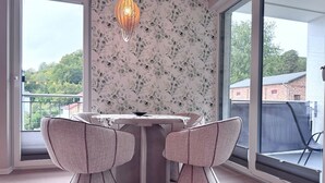 Uma área de refeições com mesa e duas cadeiras, um lustre decorativo e vista para o verde lá fora.