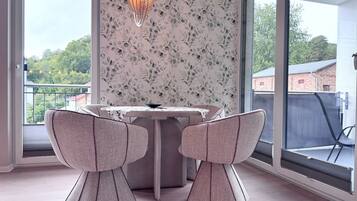 A dining area with a table and two chairs, a decorative light fixture, and a view of greenery outside.