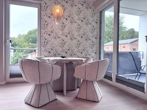 Ein Essbereich mit Tisch und zwei Stühlen, einer dekorativen Leuchte und Blick auf Grünfläche.