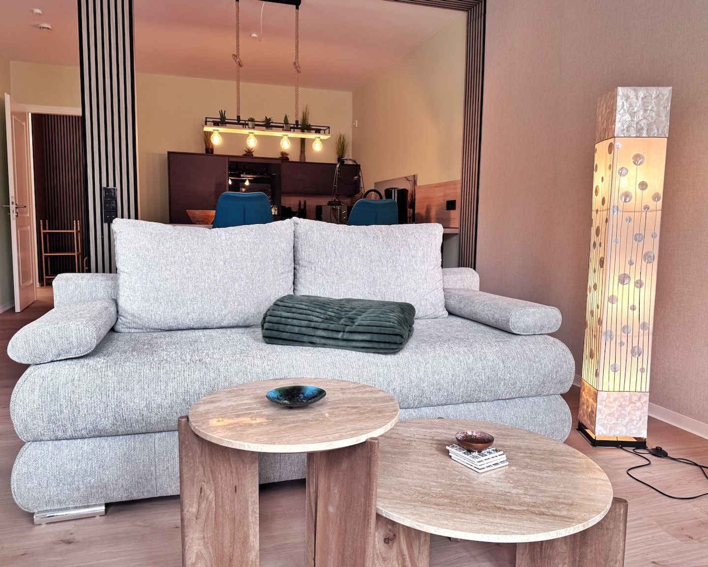 Ein modernes Wohnzimmer mit einem grauen Sofa, zwei Holztischen und einer dekorativen Leuchte.