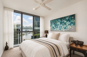 Une chambre à coucher avec un grand lit, un ventilateur de plafond, une vue sur une rivière et un tableau accroché au mur.