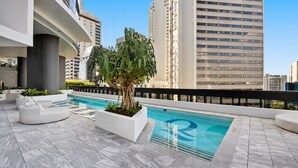 A rooftop pool area with a modern design, including a pool, lounge seating, and a large tree. - Maison Quatre | Brisbane Skyline & River Escape (Brisbane City)