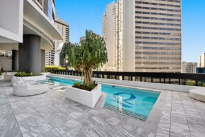 Un espace piscine aménagé sur le toit, doté d’un design moderne, comprenant une piscine, des espaces de détente et un grand arbre.