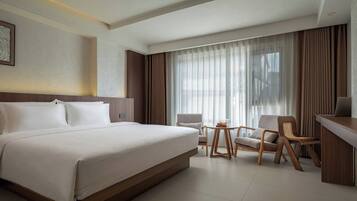 A hotel room with a large bed, a desk, a chair, and a small table.