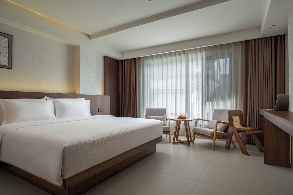 Une chambre d’hôtel avec un grand lit, un bureau, une chaise et une petite table sur laquelle se trouvent des fruits.