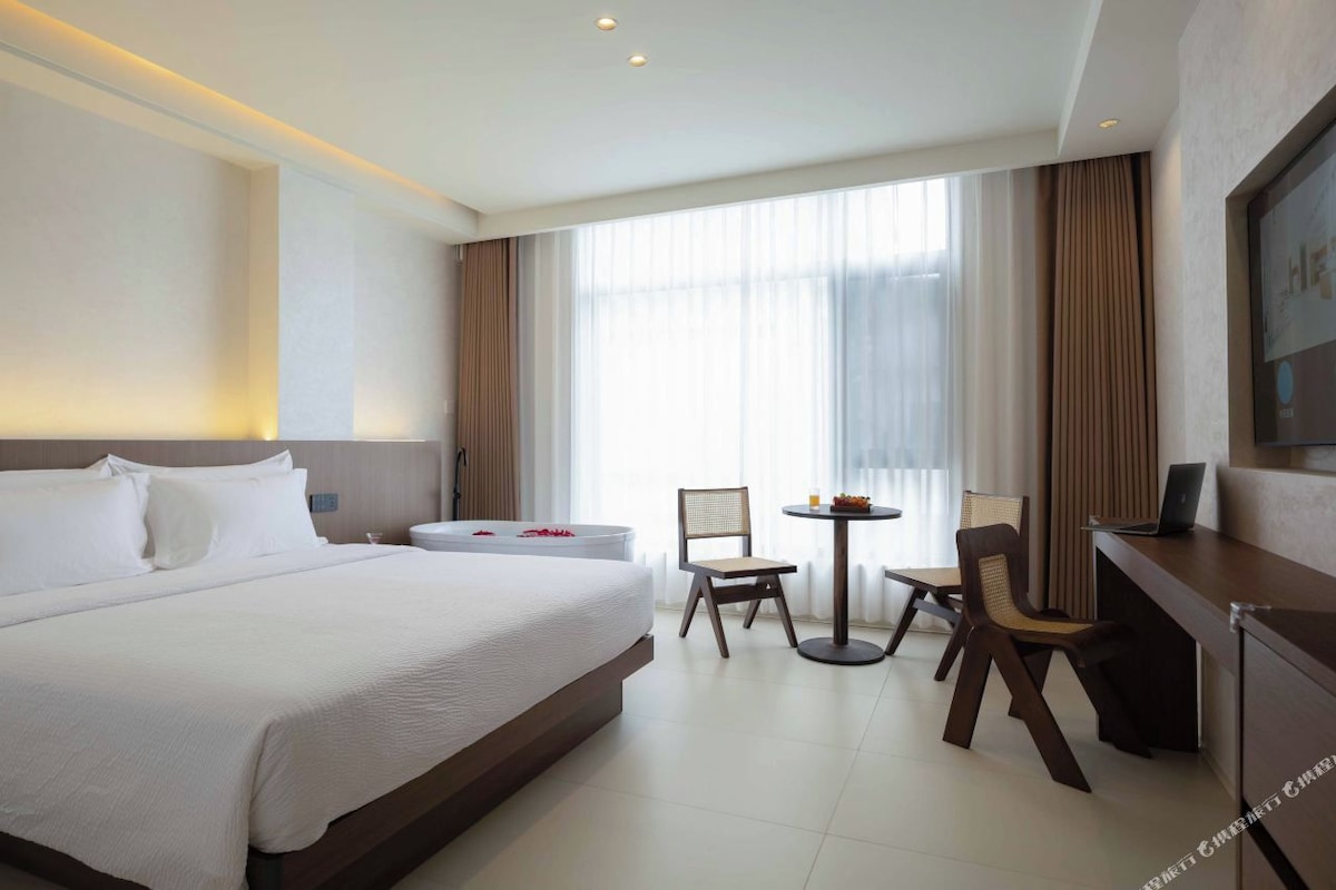 Une chambre d’hôtel avec un grand lit, un bureau avec un ordinateur portable, deux chaises et une petite table.