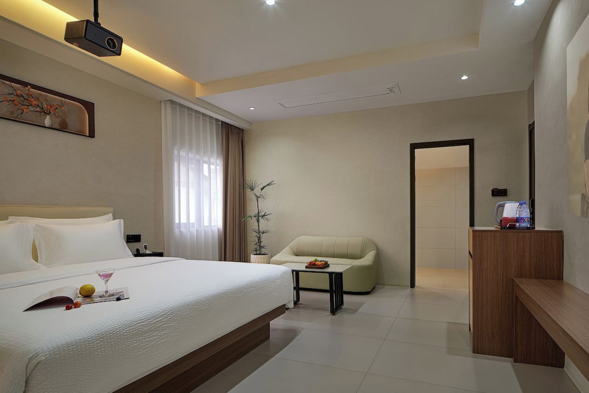Une chambre d’hôtel avec un lit, un bureau, une chaise, une plante en pot et un mini-bar.