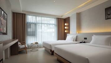 A hotel room with two beds, a desk, a chair, a small table, and a large window with curtains.