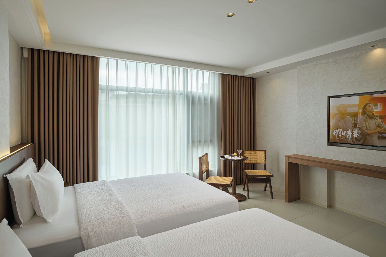 A hotel room with two beds, a desk, a chair, and a television on the wall.