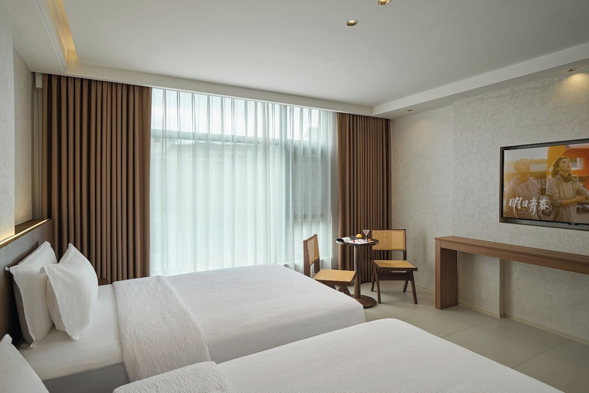 Une chambre d’hôtel avec deux lits, un bureau, une chaise et un téléviseur fixé au mur.
