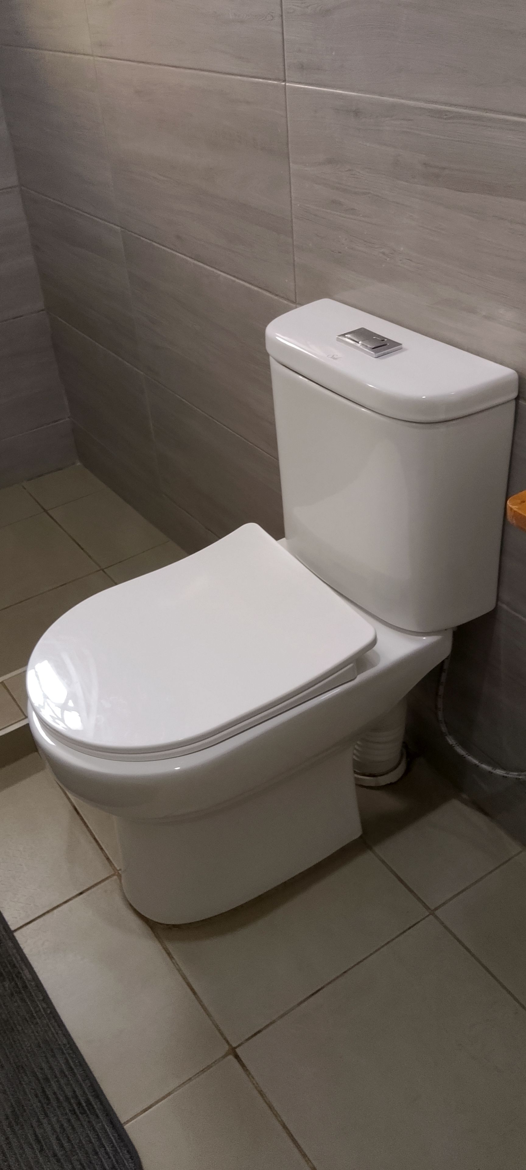 Eine weiße Toilette mit Tank und Sitz in einem Badezimmer mit gefliestem Boden und Wänden.