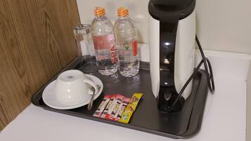 Una bandeja con una taza blanca, dos botellas de agua, un par de pantuflas y una caja de pantuflas sobre una recepción de hotel.