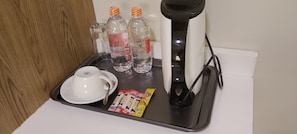 A tray with a white cup, two water bottles, a pair of slippers, and a box of slippers on a hotel counter.