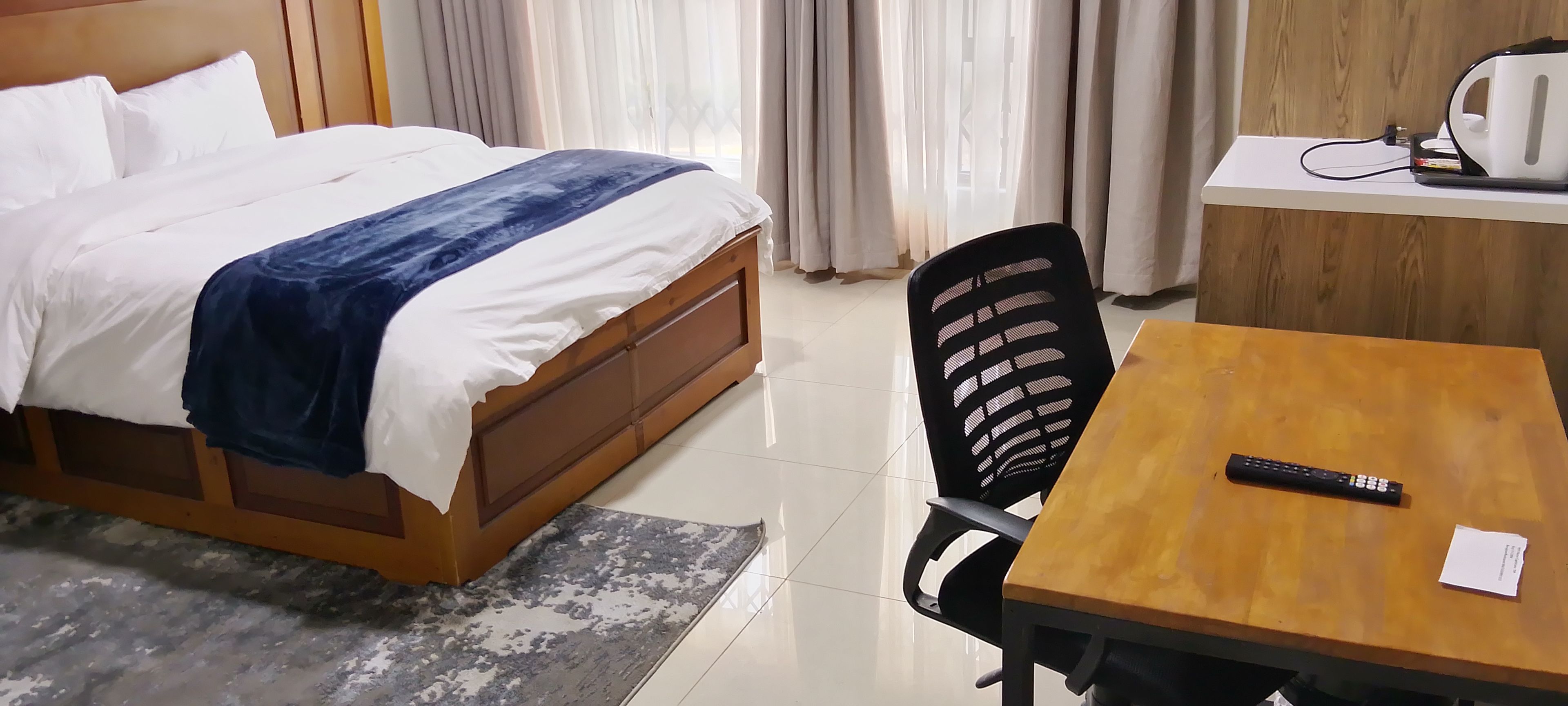 A hotel room with a bed, a desk with a kettle, and a chair.