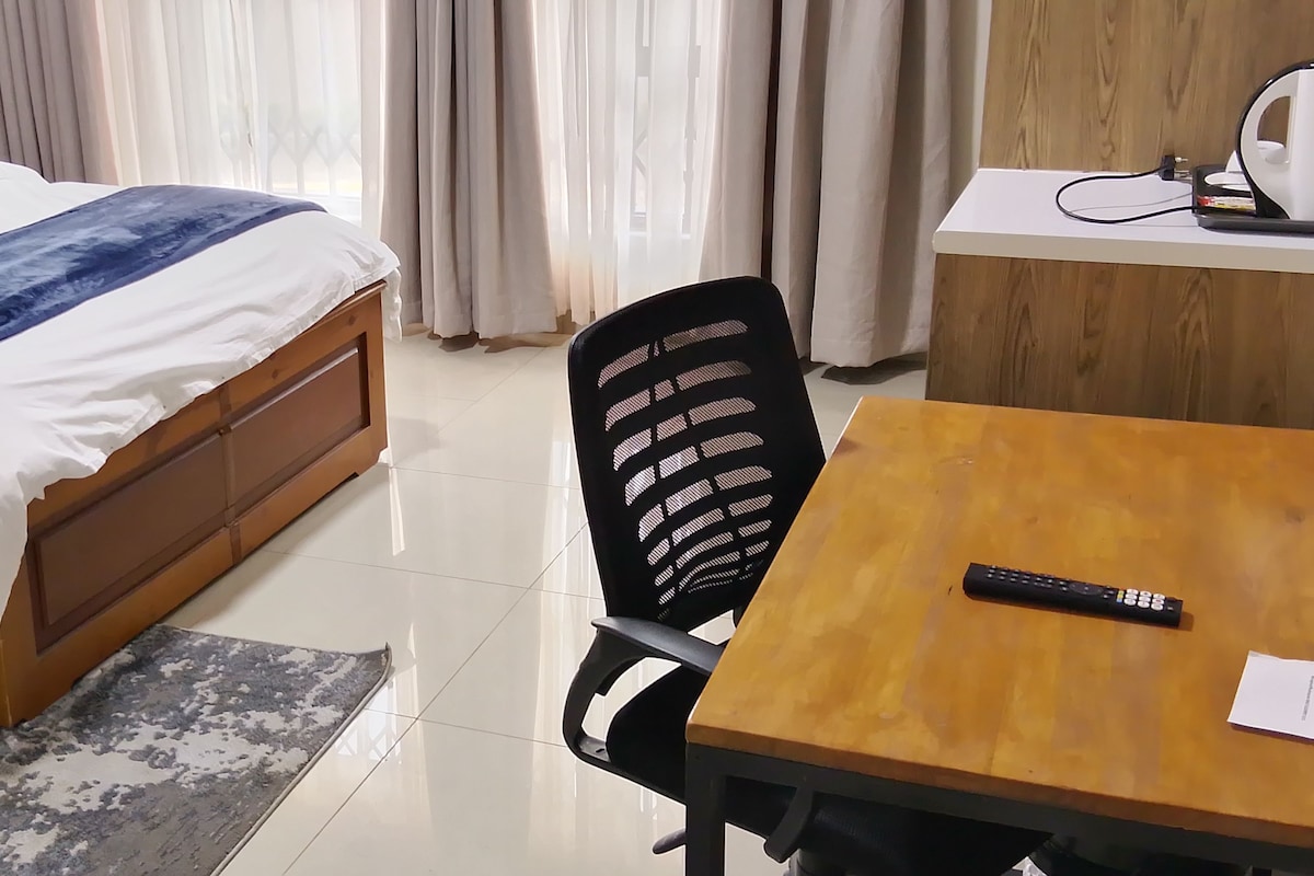 A hotel room with a bed, a desk with a kettle, and a chair.