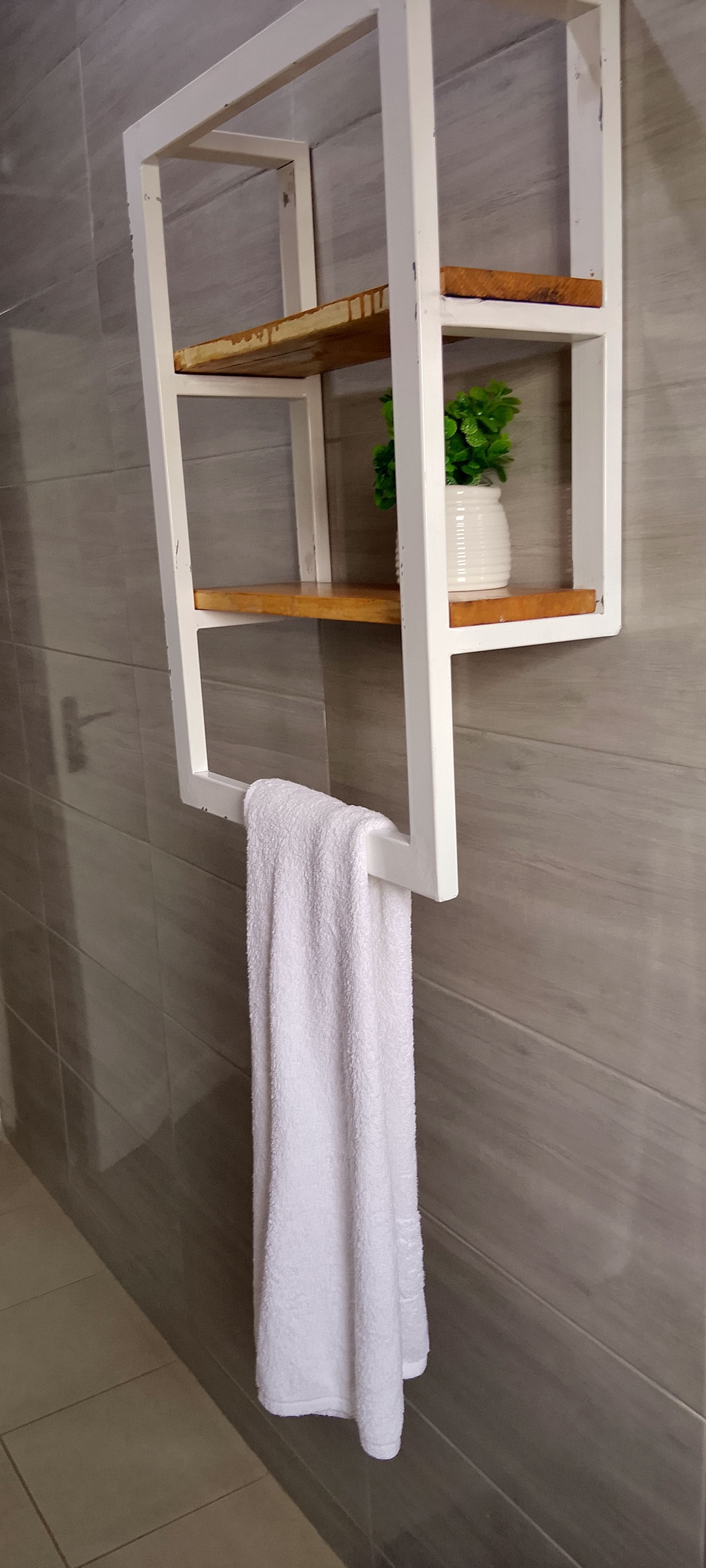 Una toalla blanca colgada en un perchero en un baño con azulejos grises.
