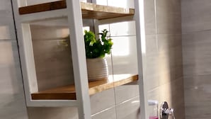Ein Badezimmer mit weißem Waschtisch, einem Handtuch an der Wand und einer kleinen Topfpflanze auf dem Regal.