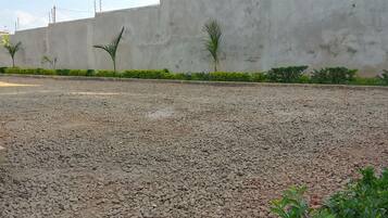 Un patio de grava con un muro de hormigón, plantas pequeñas y una verja roja.