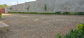 A gravel courtyard with a concrete wall, small plants, and a red gate.