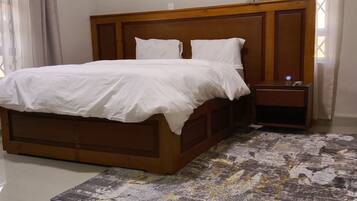 A bedroom with a wooden bed frame, white bedding, a nightstand, and a patterned rug.