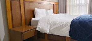 A hotel room with a wooden headboard, a single bed with white bedding, a nightstand, and a window with curtains.