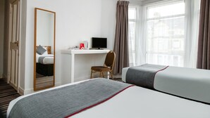 A hotel room with a bed, a desk with a computer, a chair, and a window with curtains. - Standard Double Room (Cardiff)