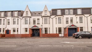A row of terraced houses with a central entrance, a car parked in front, and a clear sky. - Standard Double Room (Cardiff)
