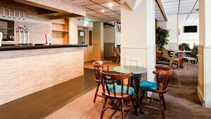 A hotel lobby with a bar area, wooden chairs, a round table, and a plant. - Standard Double Room (Cardiff)