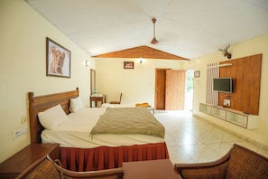 Een hotelkamer met een bed, een aan de muur bevestigde televisie, een plafondventilator en een houten hoofdeinde.