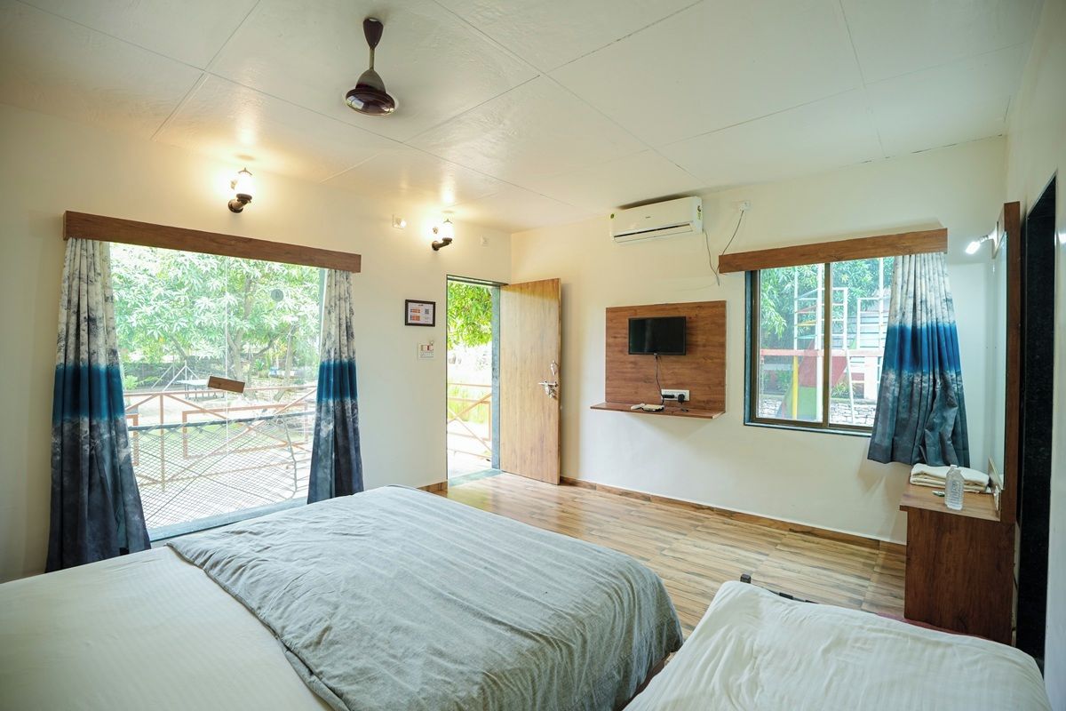 A hotel room with two beds, a television, an air conditioning unit, and a balcony with curtains.
