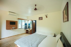 A bedroom with a bed, a mounted TV, an air conditioning unit, a ceiling fan, and a deer head decoration. - Glorious Gir Resort (Talala)