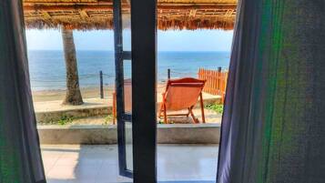 An open door leading to a beach view with a thatched roof structure, a wooden chair, and a concrete pathway.