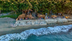 Una propiedad frente a la playa con varias cabañas de techo de paja, una playa arenosa y palmeras.