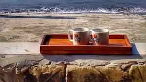 Una bandeja de madera con dos tazas frente al mar, en la playa.