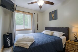 Ein Schlafzimmer mit einem Bett, einem Deckenventilator, einem Fenster mit Vorhängen, einem an der Wand befestigten Fernseher, einer Wanddekoration mit einem Hirschkopf und einem Nachttisch mit einer Lampe.