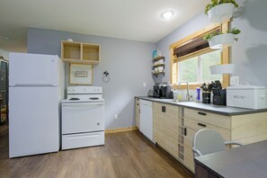 Eine moderne Küche mit weißen Geräten, Holzschränken und einem Fenster mit Blick auf Grünflächen.
