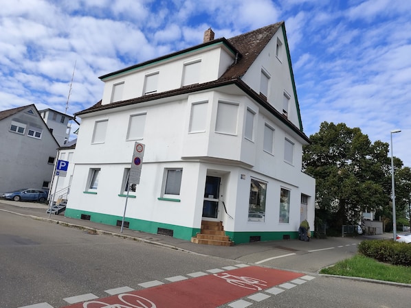 Um edifício de dois andares com fachada branca e detalhes verdes, com uma faixa de bicicleta vermelha na rua em frente.