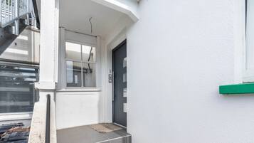 Ein weißes Gebäude mit grauer Tür, einem Fenster und einer kleinen Treppe zum Eingang.