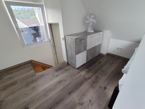 A room with a sloped ceiling, a window, a fan, and a built-in cabinet with drawers. - City Center Attic Apartment with Castle View and Wi-Fi (Heidenheim an der Brenz)