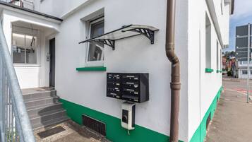 Ein Gebäude mit weißer und grüner Fassade, einer Metalltreppe, einem Briefkasten und einer Überwachungskamera.