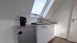 Una kitchenette compacta con lavavajillas integrado, cafetera y ventana sobre el lavadero.