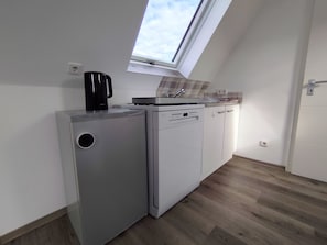 Uma kitchenette compacta com máquina de lavar louça embutida, cafeteira e janela sobre a pia.