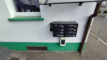 A utility box with a green base and a white wall, next to a window with a metal guard.