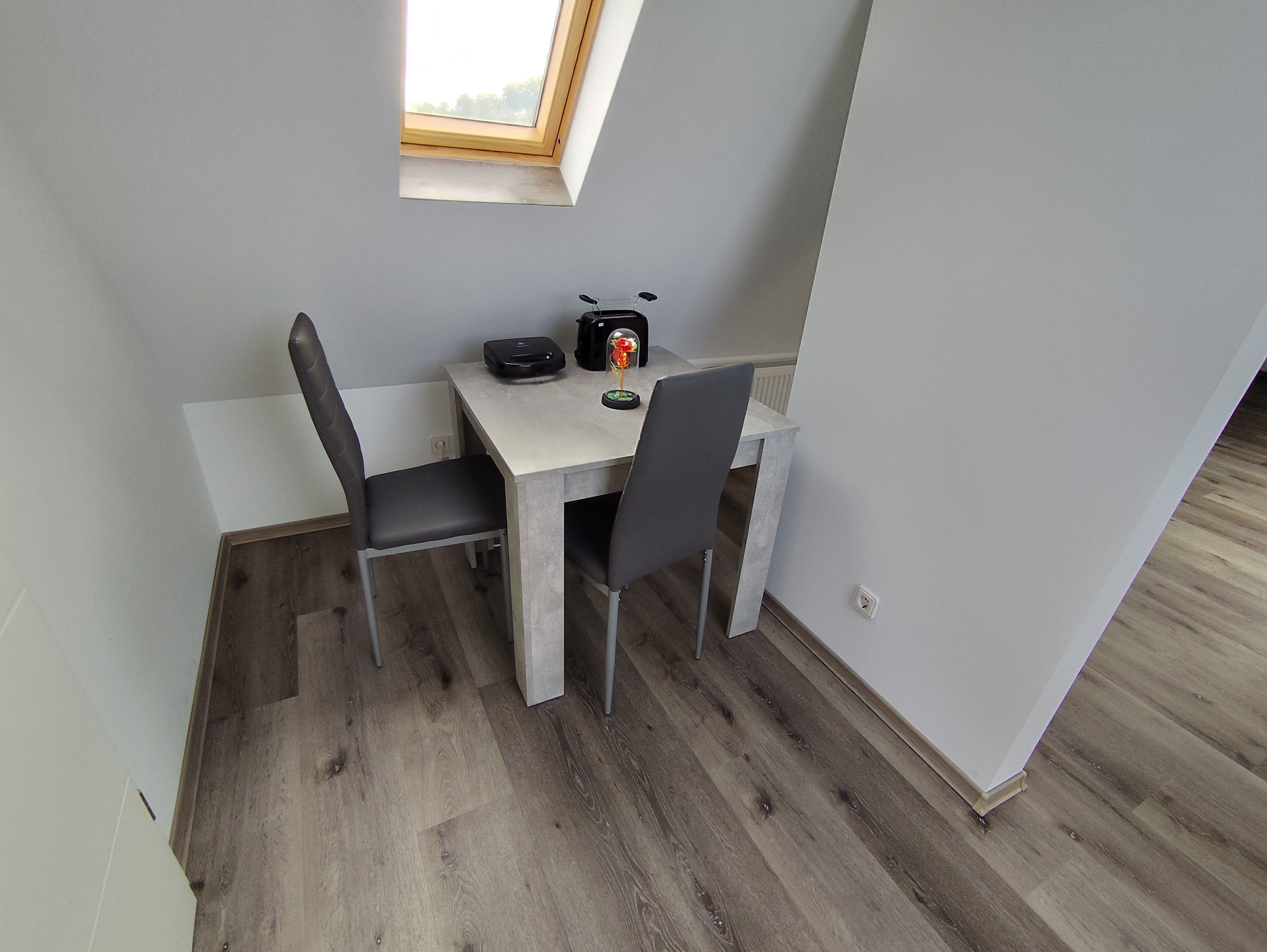 Een kleine eethoek met een tafel, twee stoelen, een koffiezetapparaat en een dakraam.