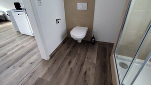 Baño con inodoro, ducha y piso de madera.
