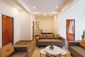 A modern living room with a sofa, two armchairs, a coffee table, and a dining area with a table and chairs. - Windsor by Redolive 15min Bagmane Tech Park 3bhk (Bengaluru)