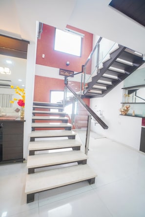 A staircase with a glass railing leading to an upper floor, a window, and a vase with flowers on the landing. - Mosaic by Redolive 4bhk Nr Gachibowli Nr Hitec (Hyderabad)